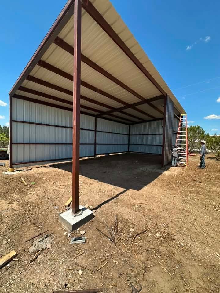 Partially built metal shed frame with corrugated roof on a dirt lot under a blue sky