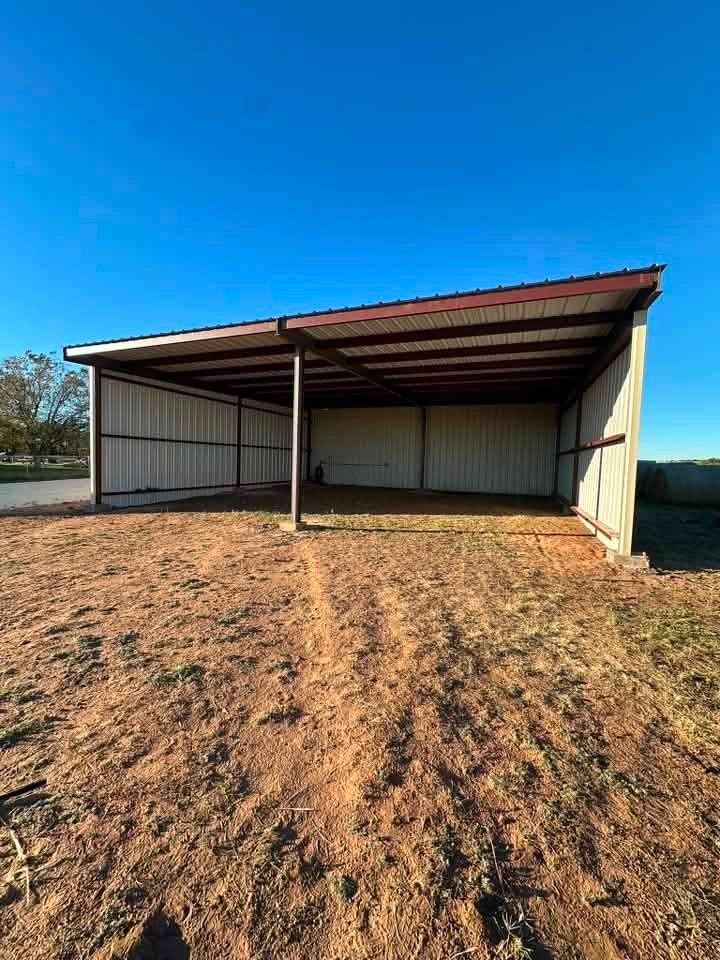 Empty metal carport on a dirt lot under a bright blue sky