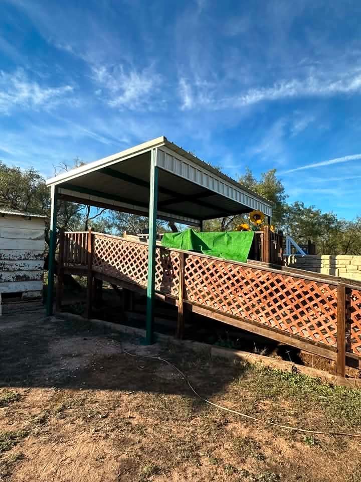 Covered walkway with lattice railing beside a small metal-roofed structure under a blue sky