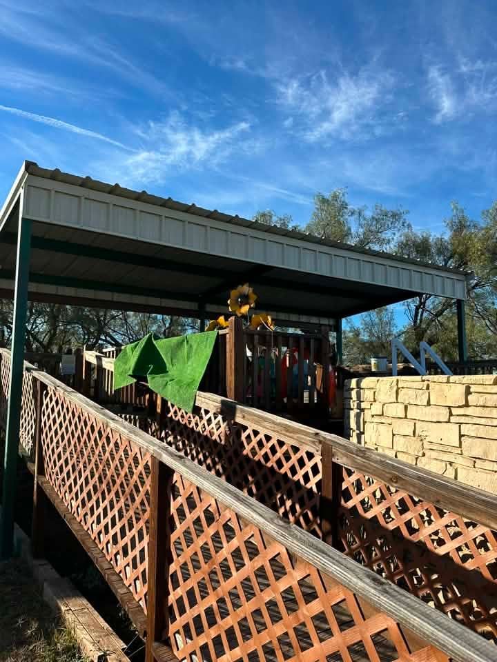 Backyard deck with lattice railing, green cloth, stone wall, and a metal-roofed patio under a blue sky