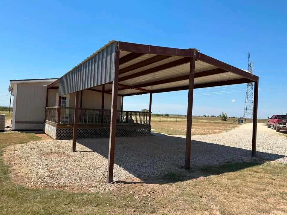 Metal carport attached to a small house in a gravel yard under a clear sky