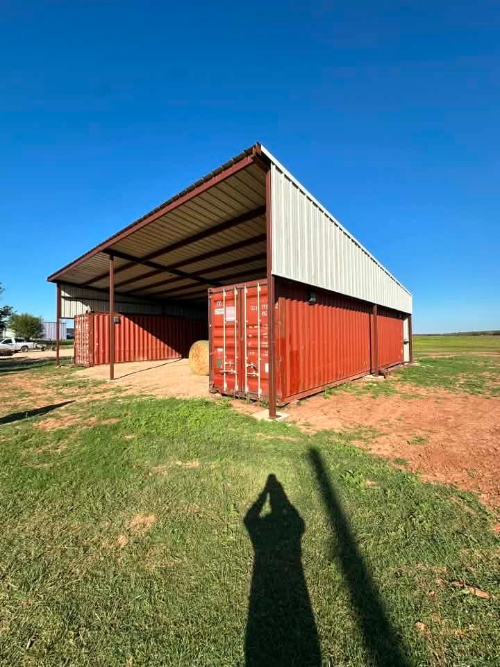 Red shipping-container barn with open front on grassy field under a clear blue sky