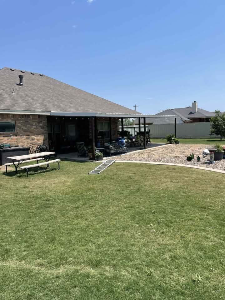 Backyard with a brick house, picnic table, lawn, and raised rock landscaping under a clear blue sky