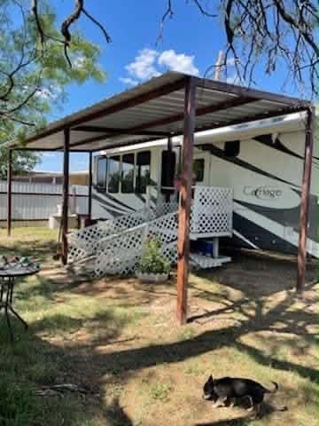 Mobile home with metal carport, small porch, and a black dog resting in the yard under trees.