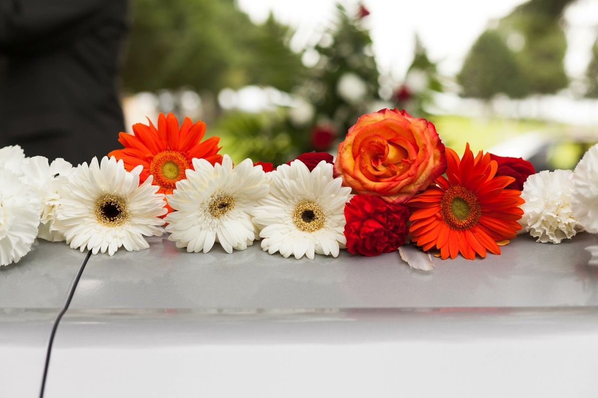 Flower arrangement of white, orange, and red blooms laid across a white coffin at a funeral