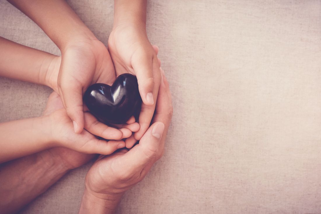 Hands gently holding a small black heart against a soft pink background