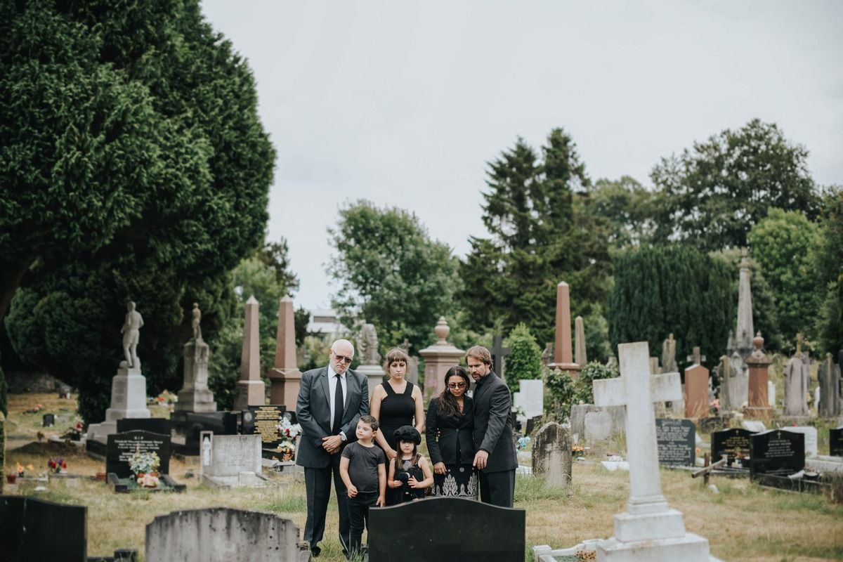People standing among gravestones in a cemetery, with trees and monuments in the background