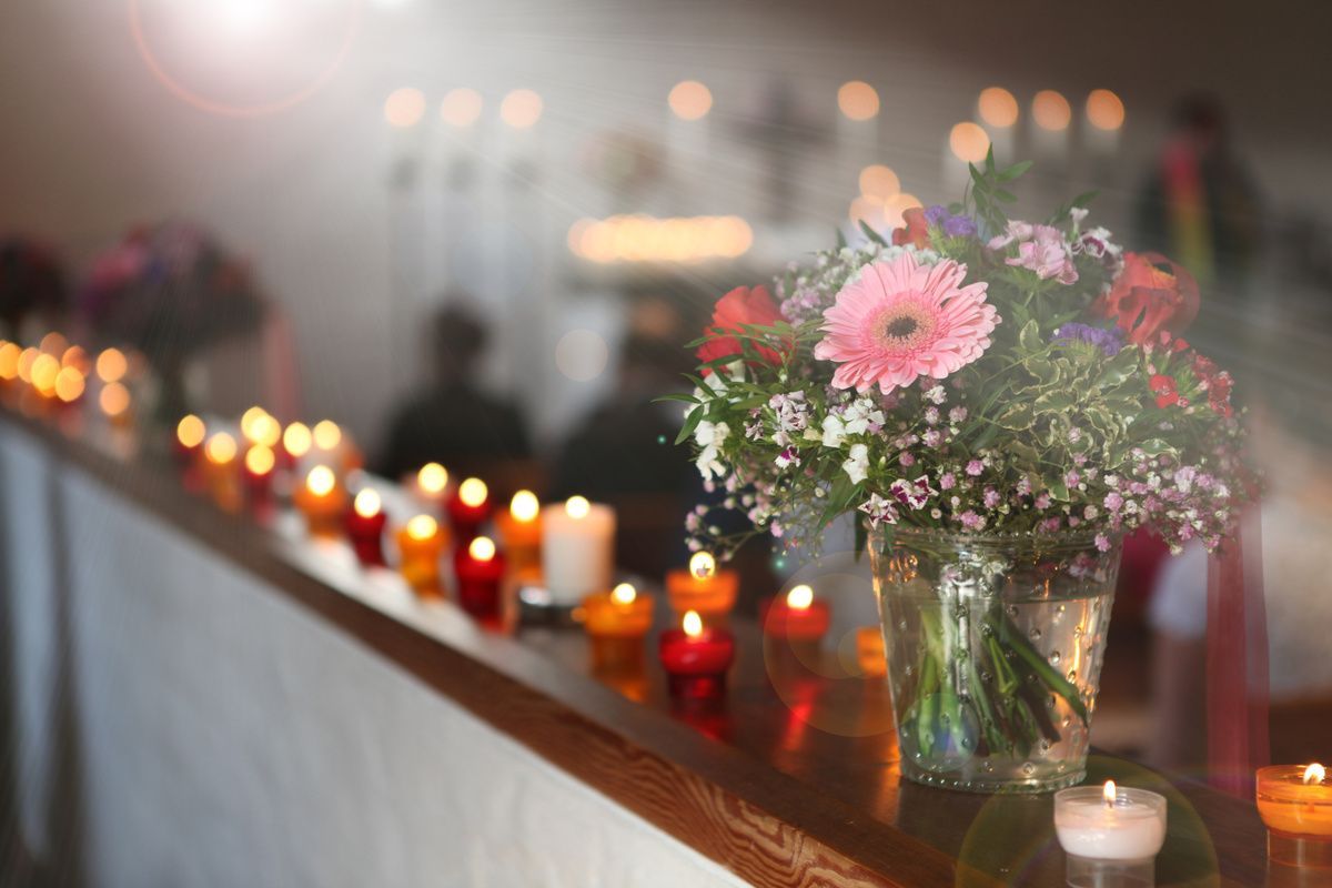 Candles and pink flowers line a memorial table in a softly blurred indoor setting