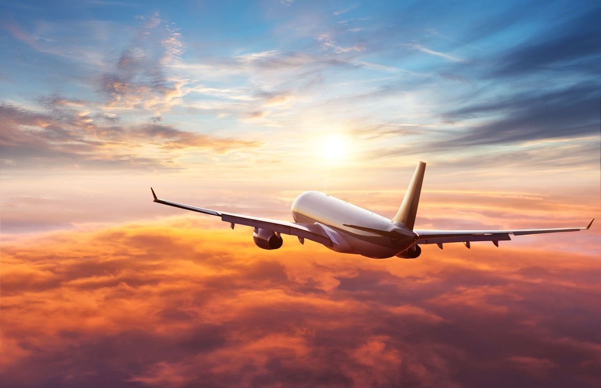 Airplane flying above orange clouds at sunset with a blue and pink sky