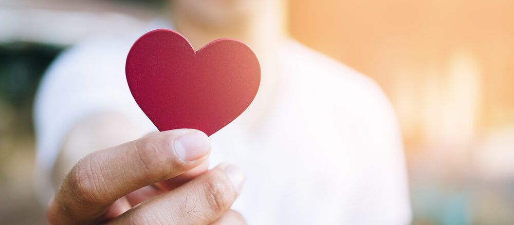 Hand holding a red heart-shaped cutout against a blurred light background