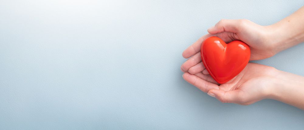 Hands holding a red heart-shaped object on a light blue background