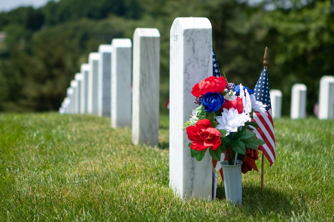 Row of white gravestones with red, white, and blue flowers and a small American flag in a cemetery