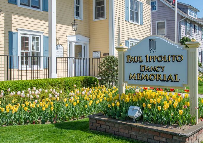 Dolc Lifpolito Dancy Memorial sign beside yellow flowers and a beige building