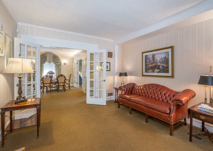 Elegant living room with a brown leather sofa, lamp, framed art, and open doors to a dining area.