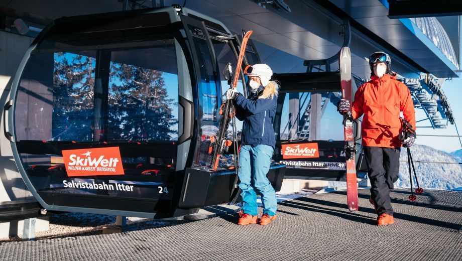 A man and a woman are standing next to a ski lift holding skis.