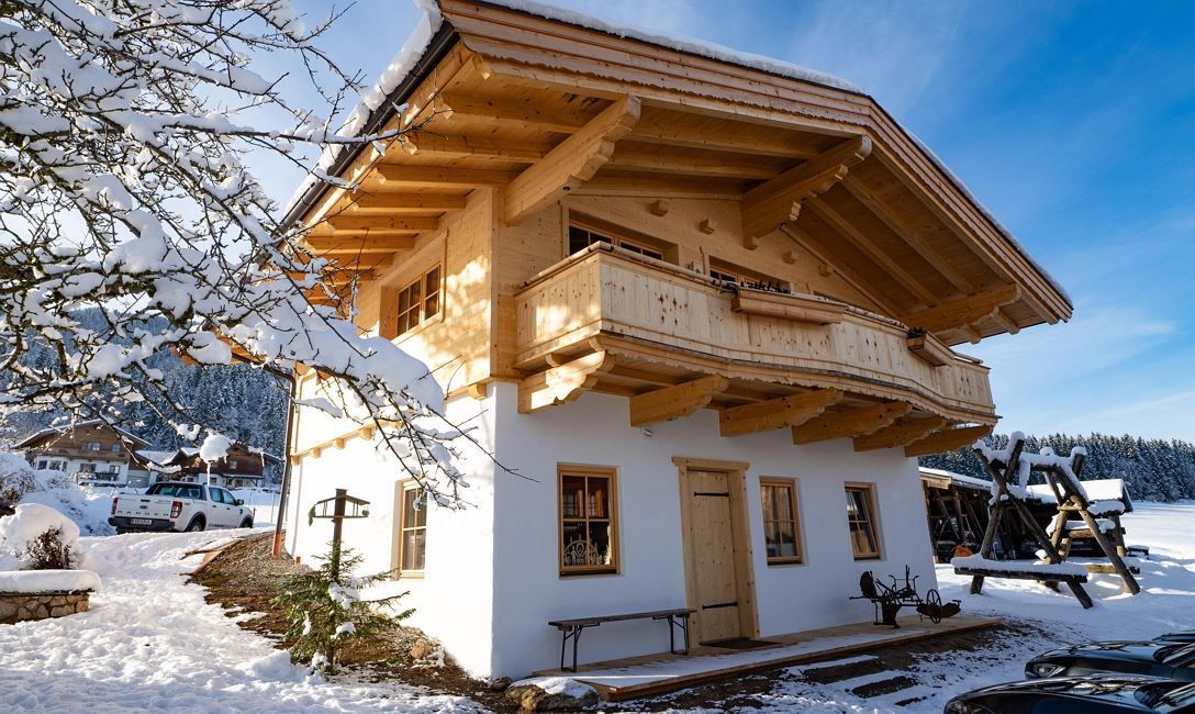 A small white house with a wooden roof is covered in snow.