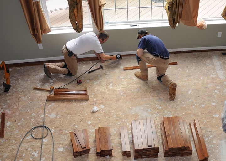 Two men are working on a wooden floor in a room.