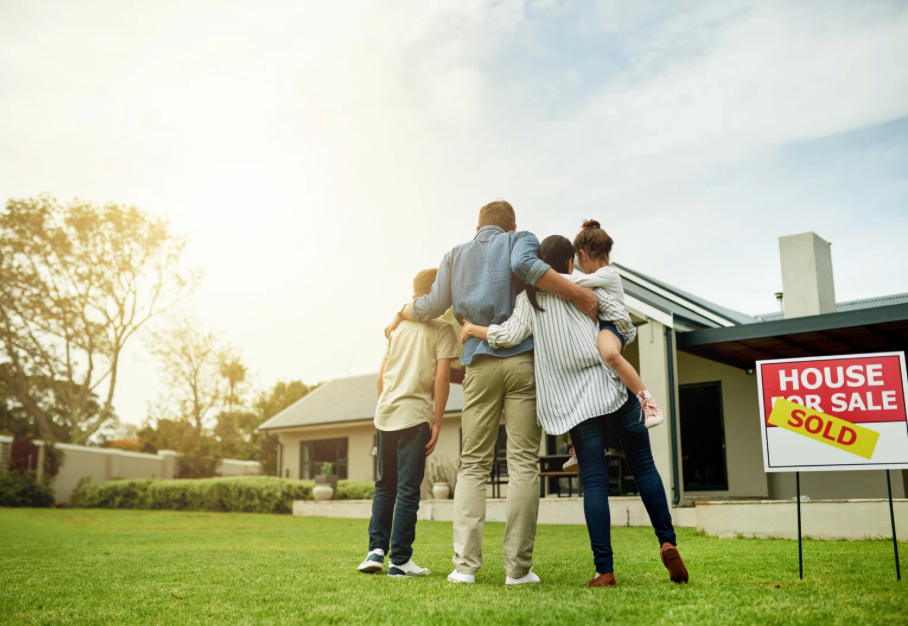 Group of people celebrating outside a house for sale with a SOLD sign in the yard.