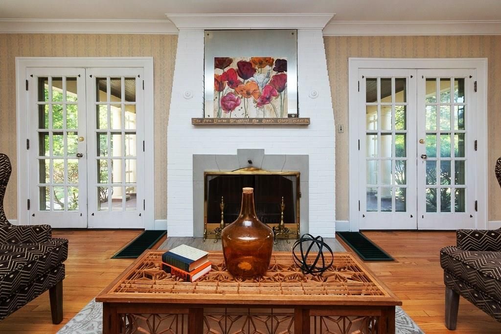 Bright living room with white fireplace, colorful art, French doors, and a wooden coffee table with decor.