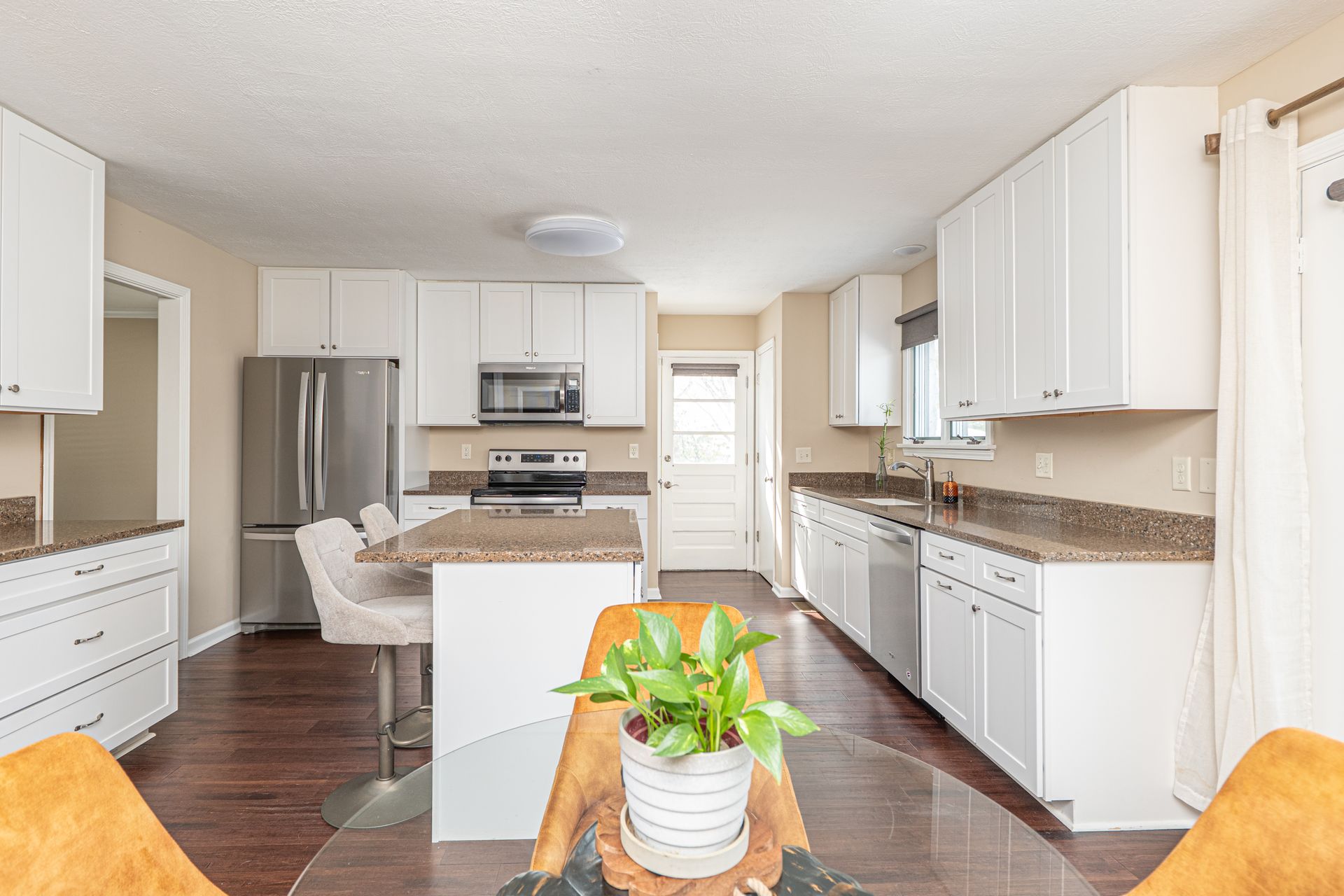 Bright modern kitchen with white cabinets, granite counters, stainless steel fridge, and central island with flowers