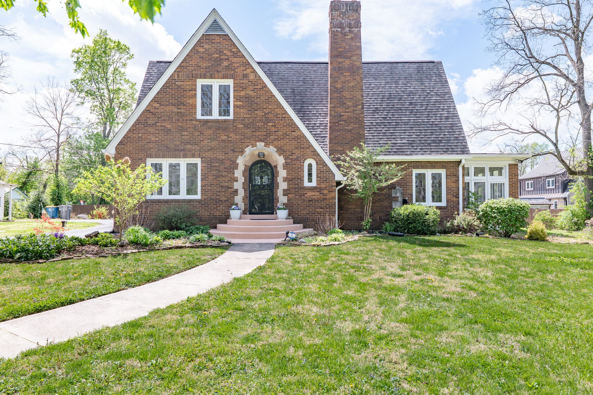 Brick house with steep roof, front porch, and curved walkway in a sunny yard.