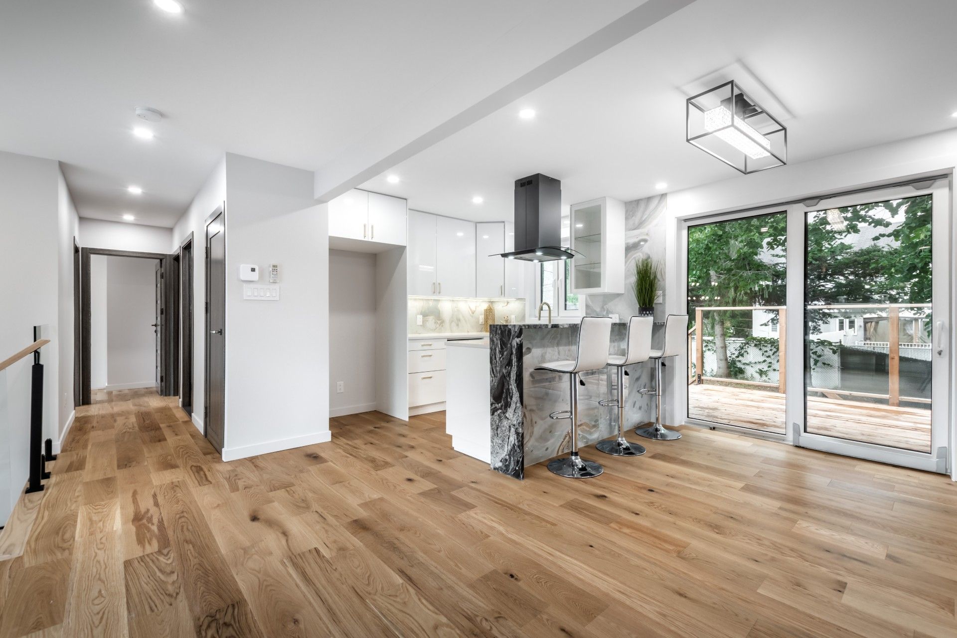 Modern open-plan living room with wood floors, kitchen island, and large sliding glass doors to a patio.