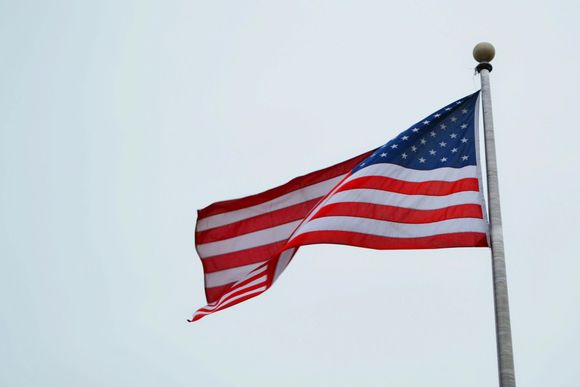 American flag waving on a flagpole against a light blue sky.