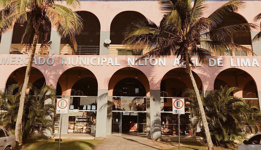 Exterior do Mercado Municipal Nilton Abel de Lima, de cor rosa, com entradas em arco e palmeiras ao redor.