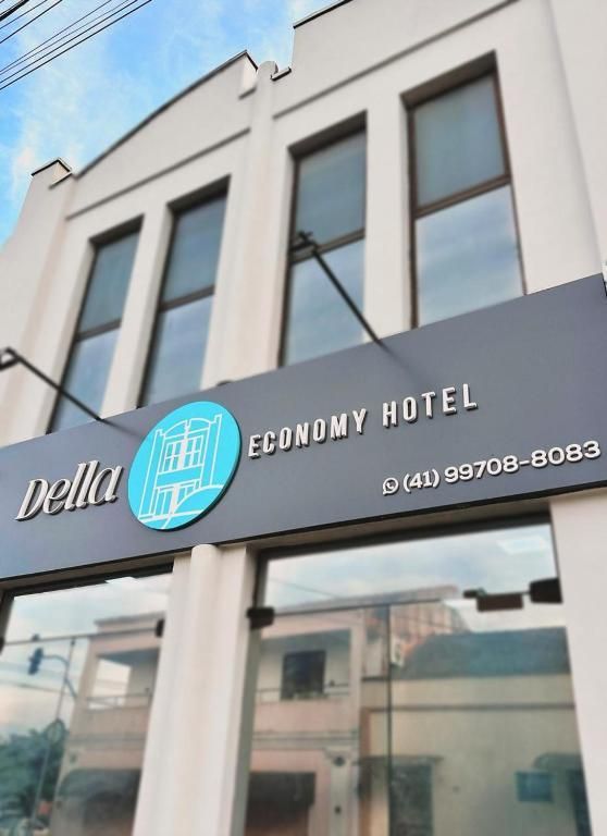 Placa do Della Economy Hotel na fachada branca de um prédio, com um número de telefone, vista de um ângulo baixo sob um céu azul.