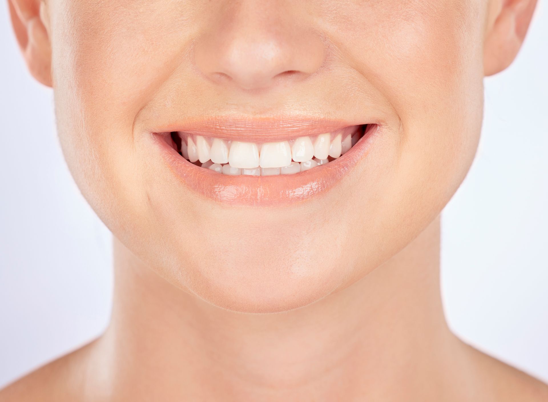 Close-up of a smiling mouth with white teeth and glossy pink lips