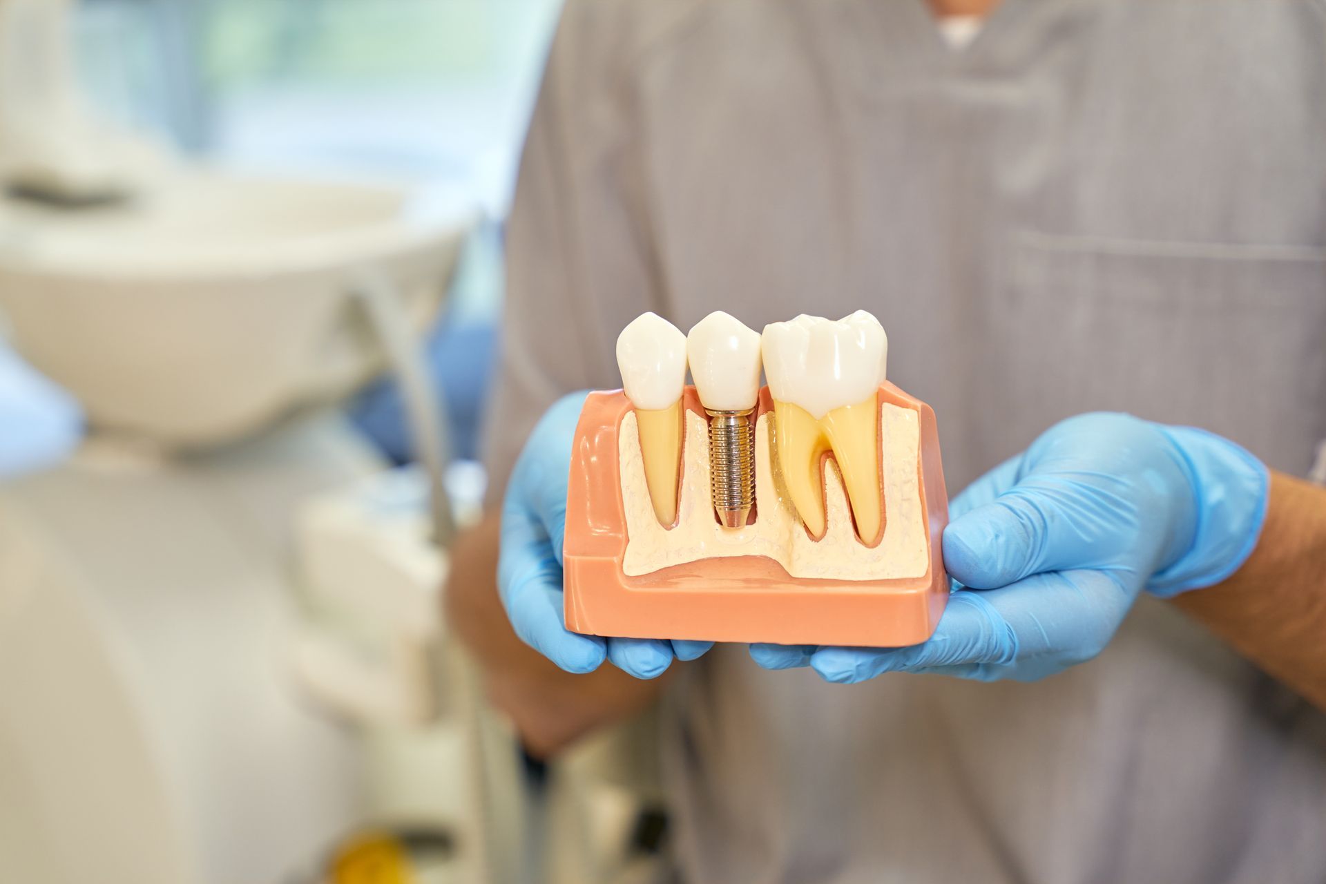 Dentist holding a model of a tooth and dental implant in a dental office.
