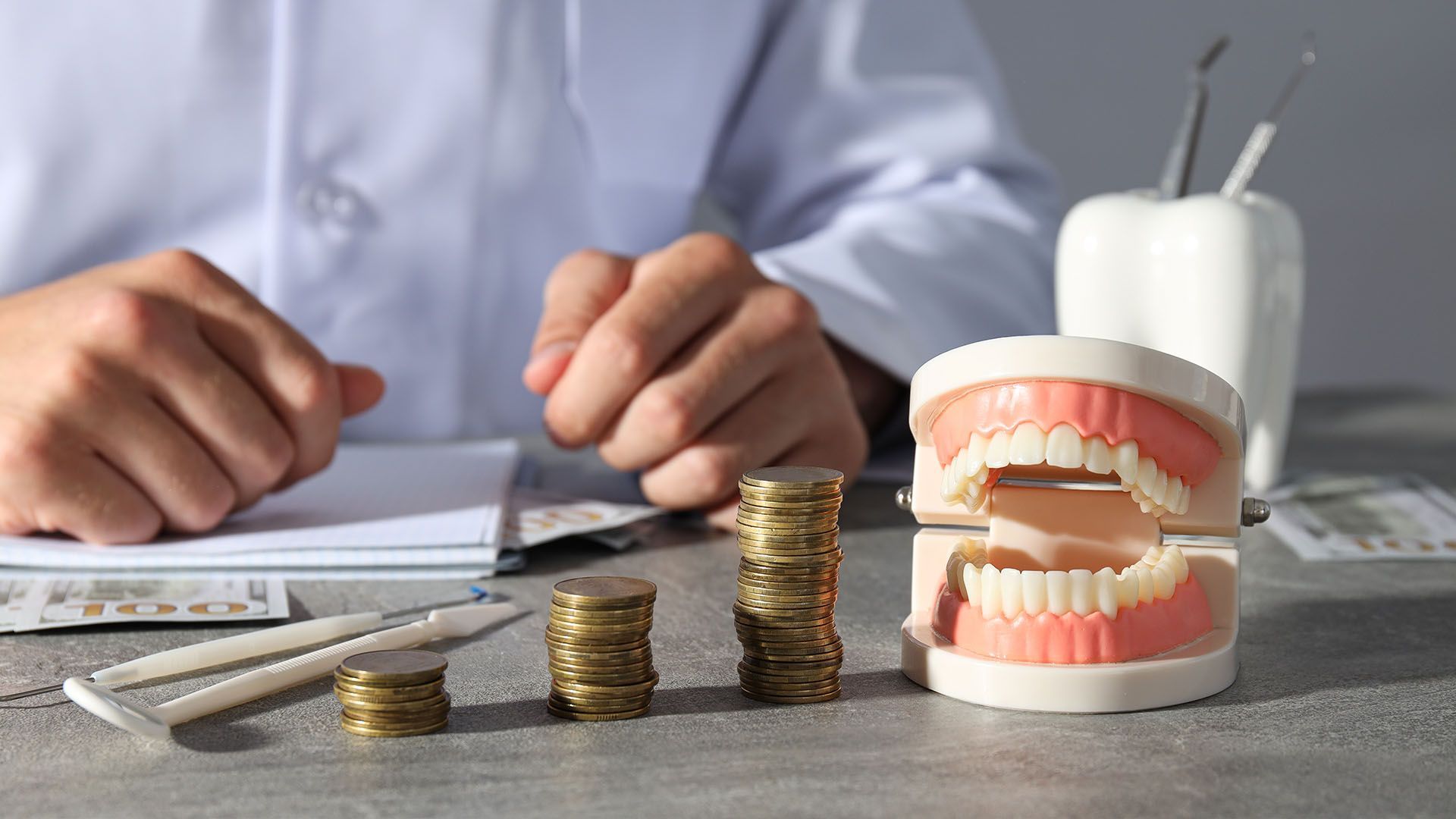 Dentist with stacks of coins and teeth model on table.