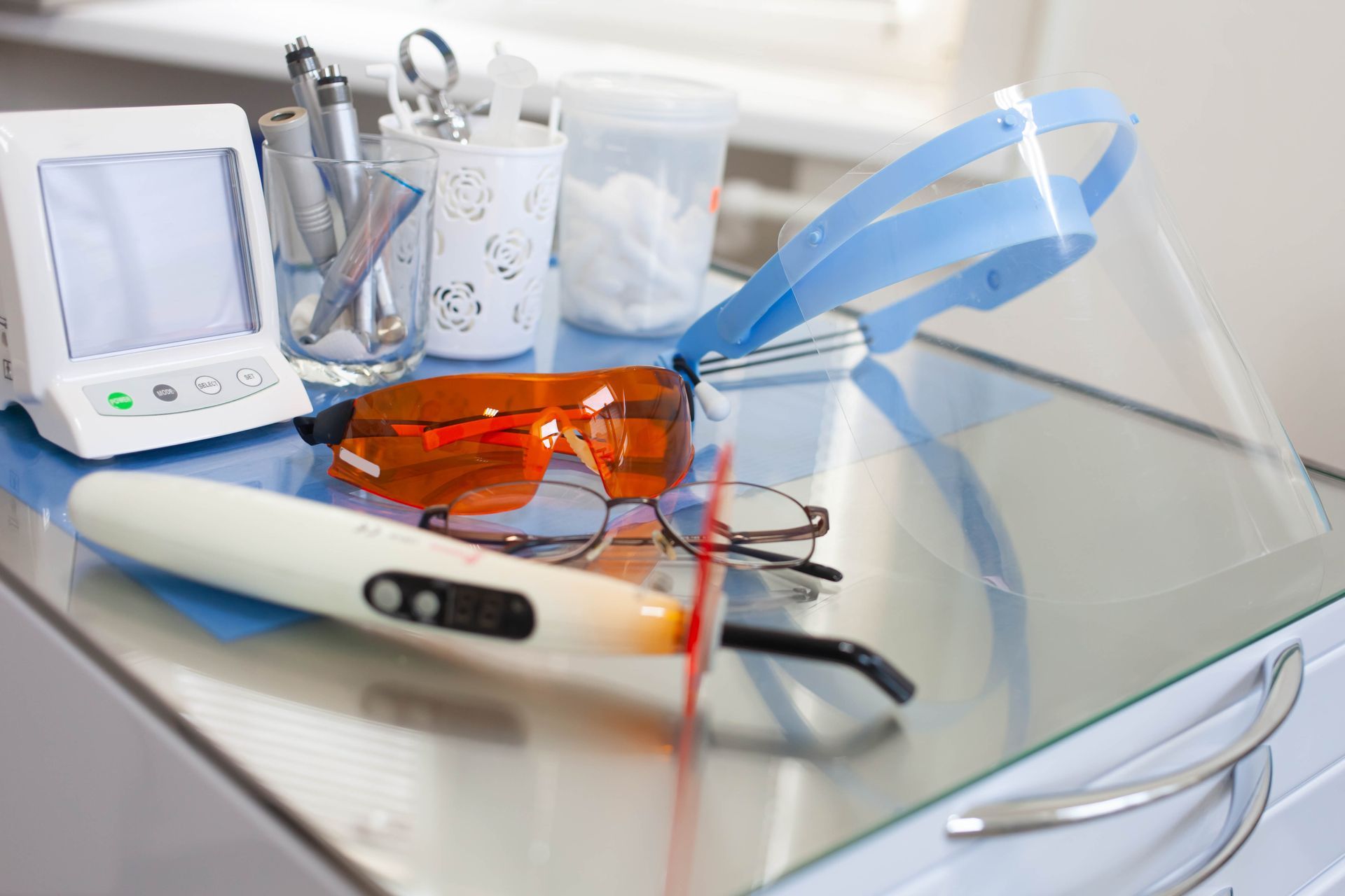 Dental tools with orange protective glasses and a blue face shield on a clinic tray