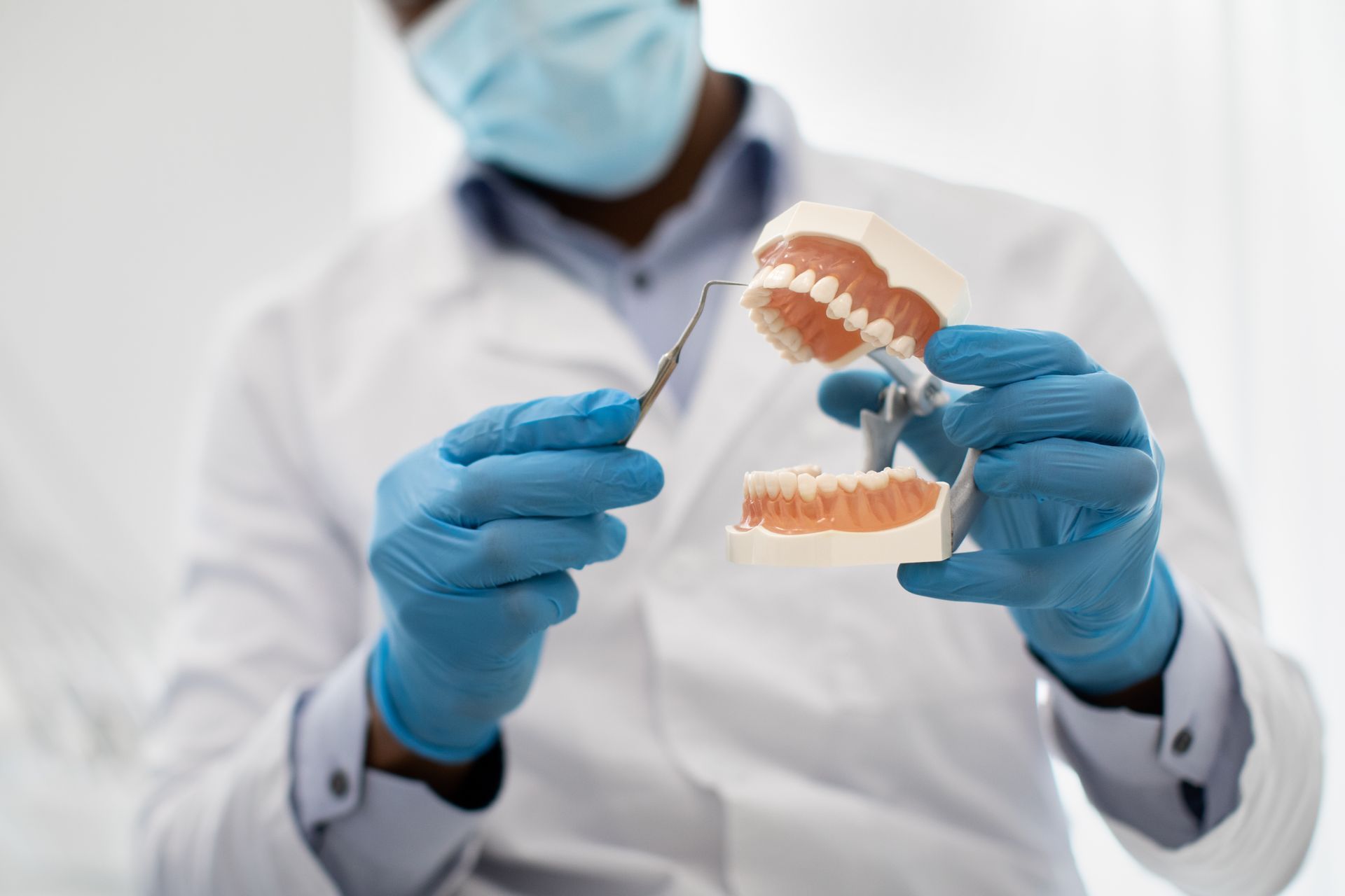 Dentist in white coat and blue gloves holding dental model and tools in a clinic