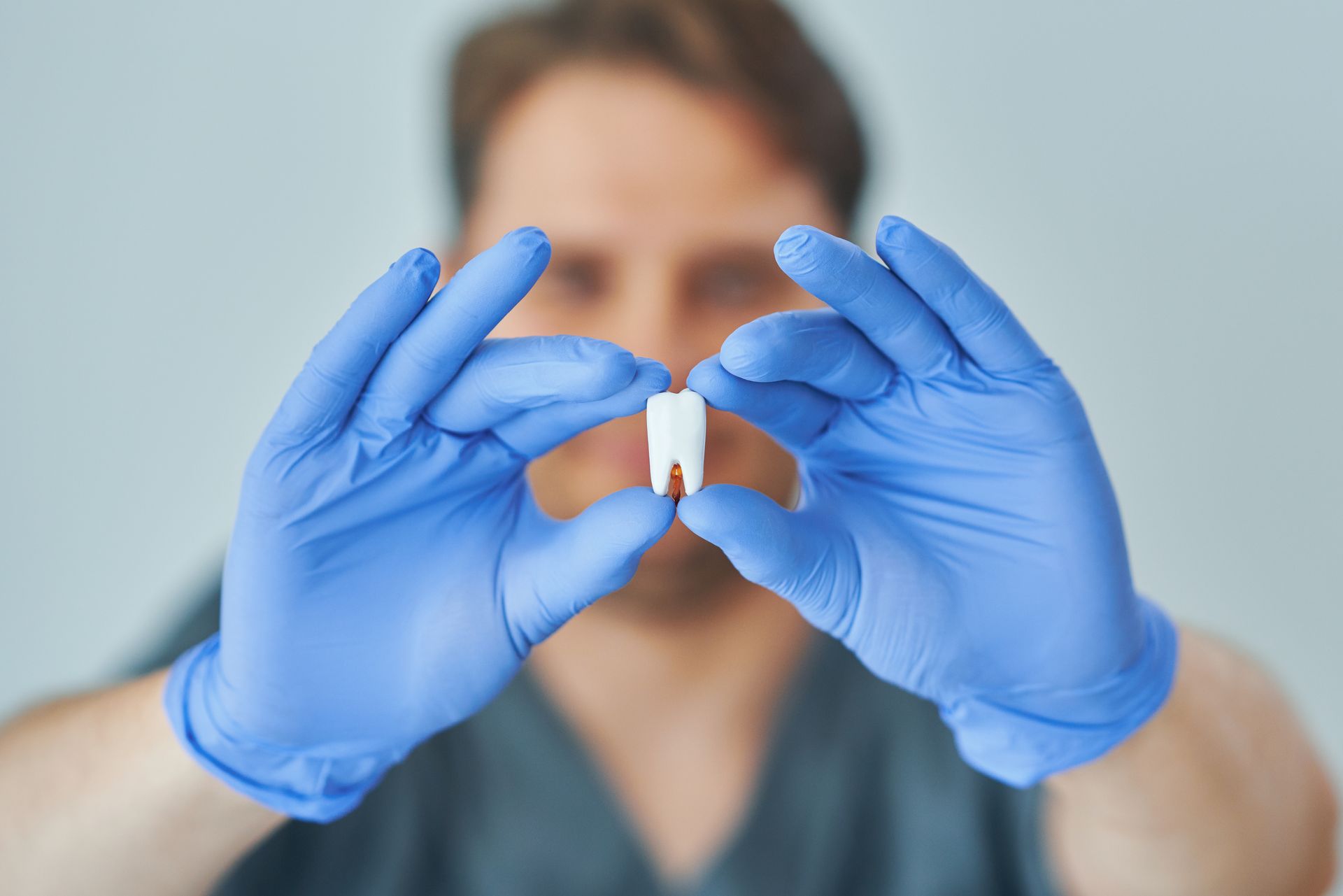 Person in blue gloves holding a small vial in front of a blurred face