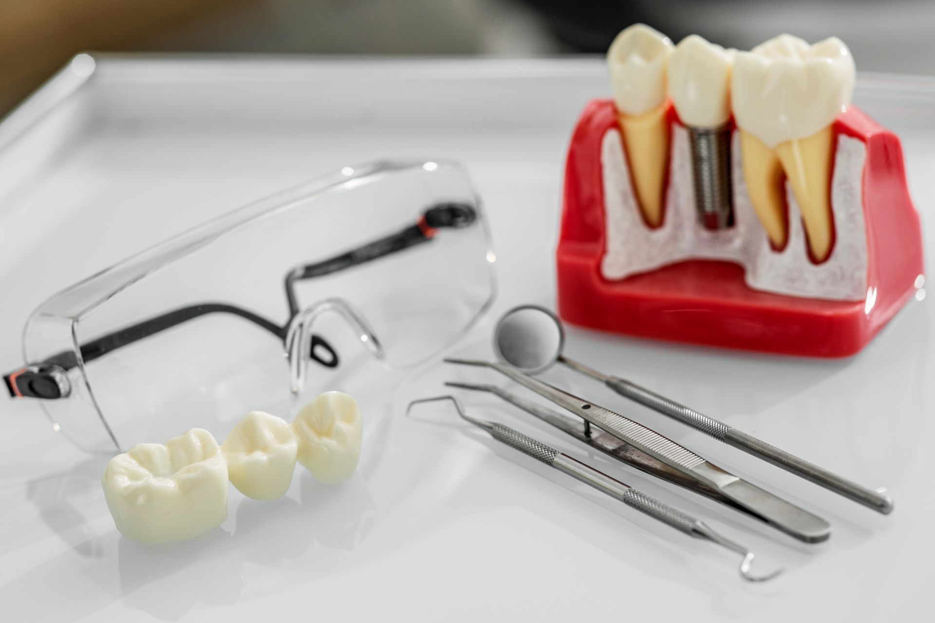Dental tools and model teeth on a white surface with safety glasses.