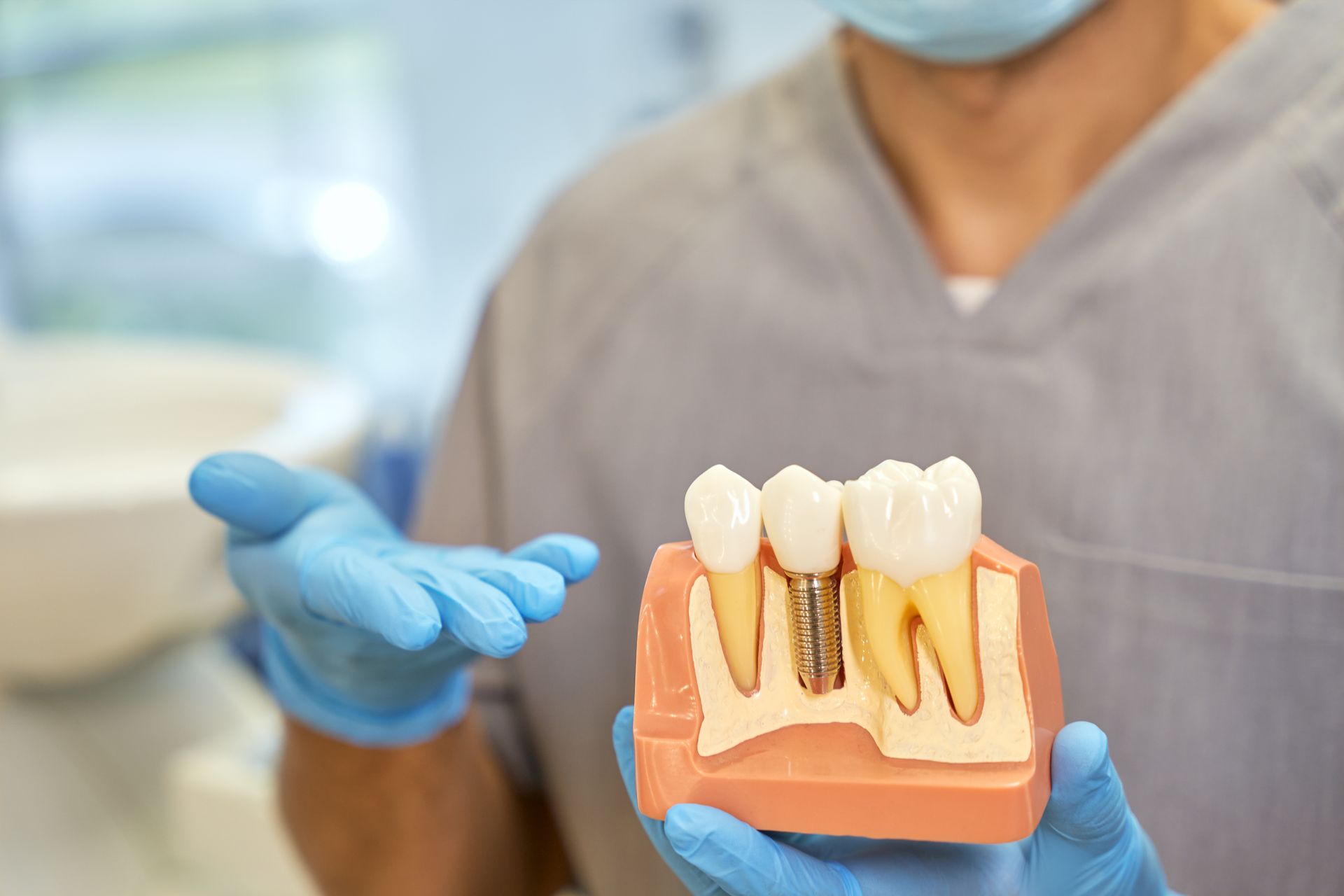 Dentist holding a model of teeth with dental implants while wearing blue gloves and a mask