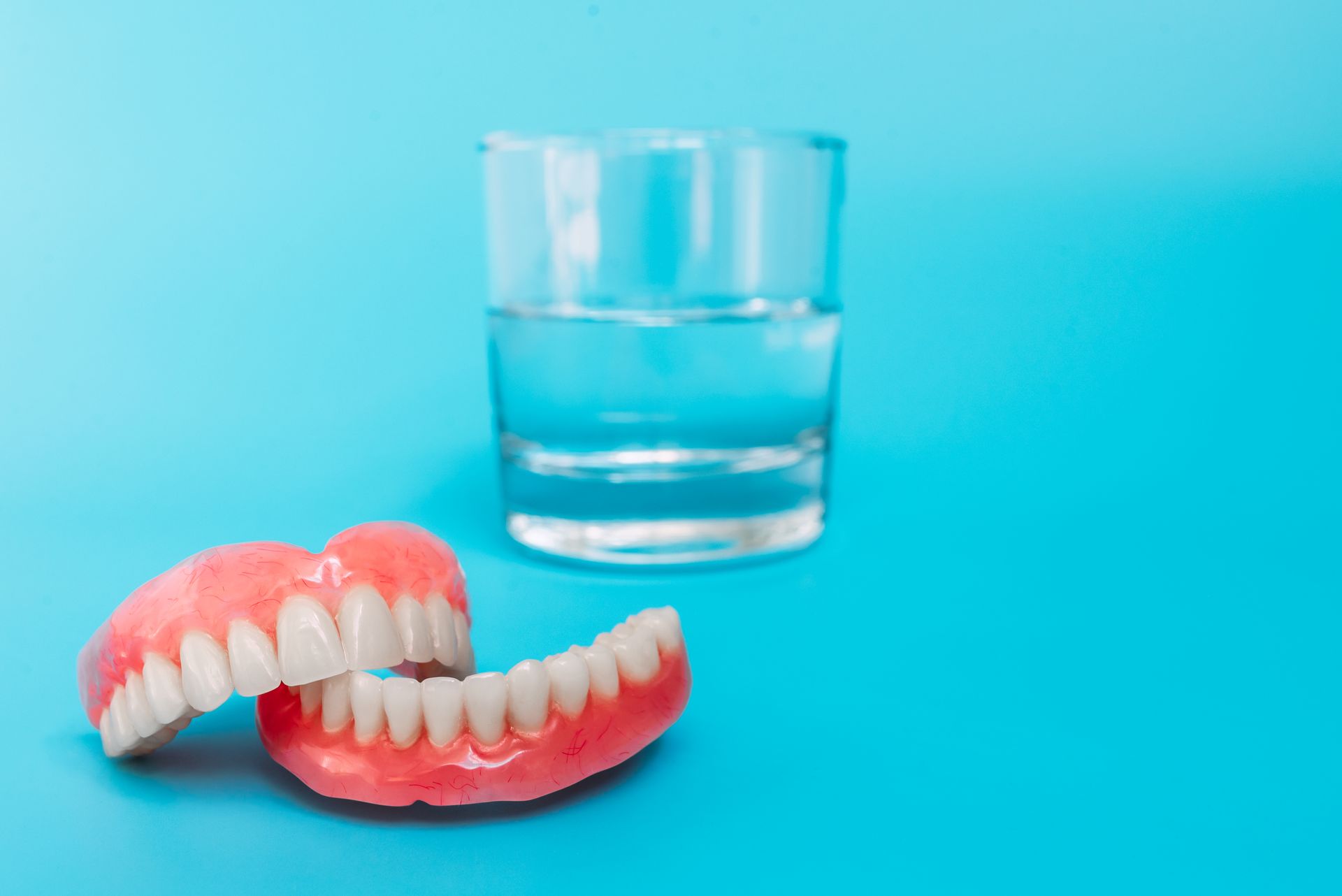 Dentures beside a glass of water on a blue background