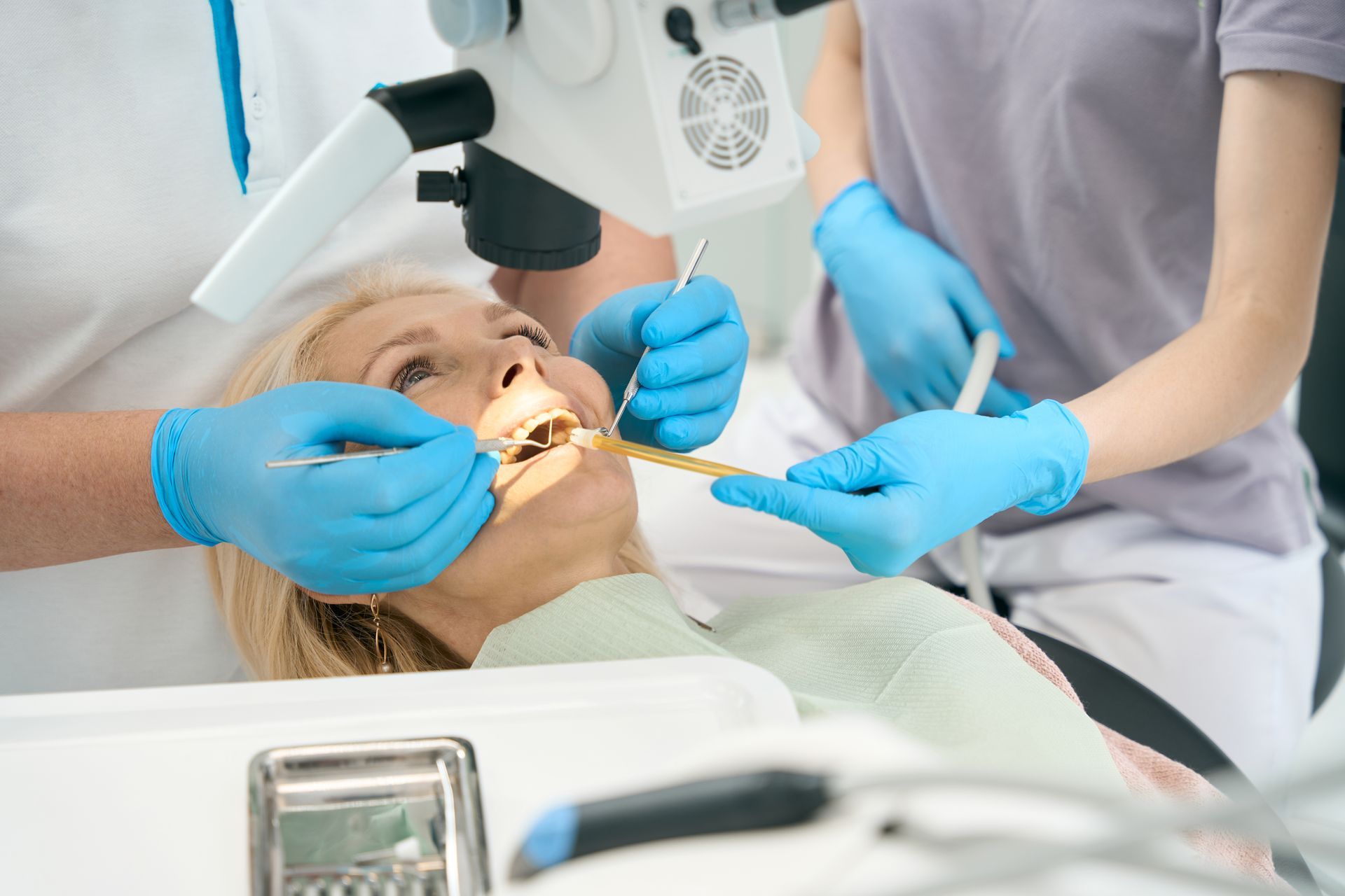 Dentist examining a patient's mouth with tools and a microscope; dental office setting.