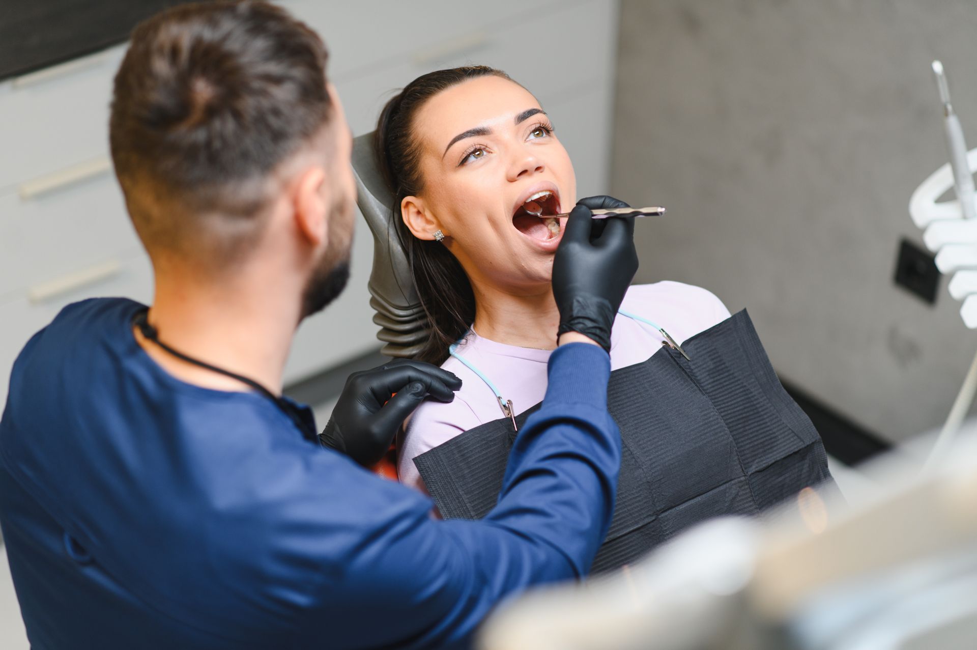 Dentist examining a patient in a dental chair, using a tool while she opens her mouth