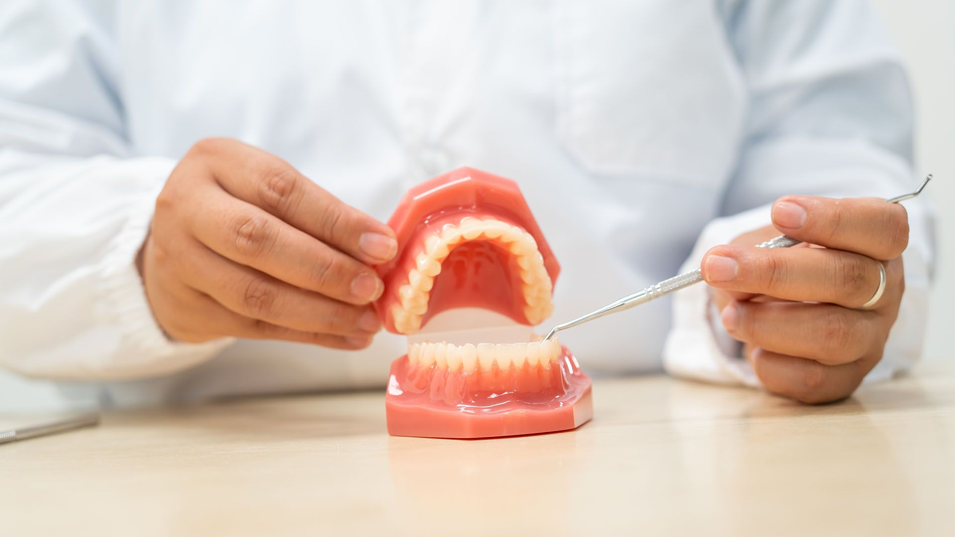 Dentist holding upper and lower dentures, using a dental tool on a table.