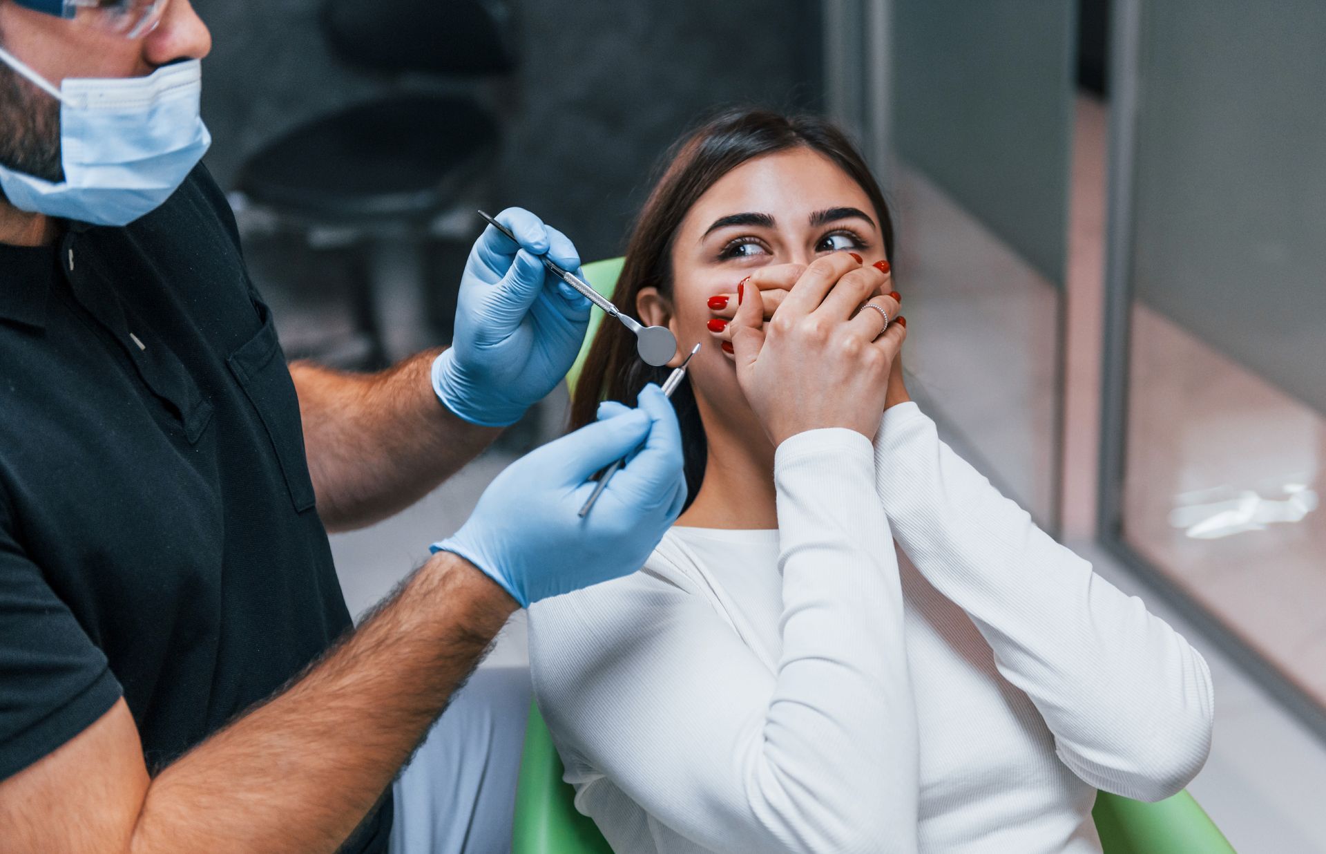 Dental clinic scene: patient in white covers mouth while dentist in gloves administers treatment