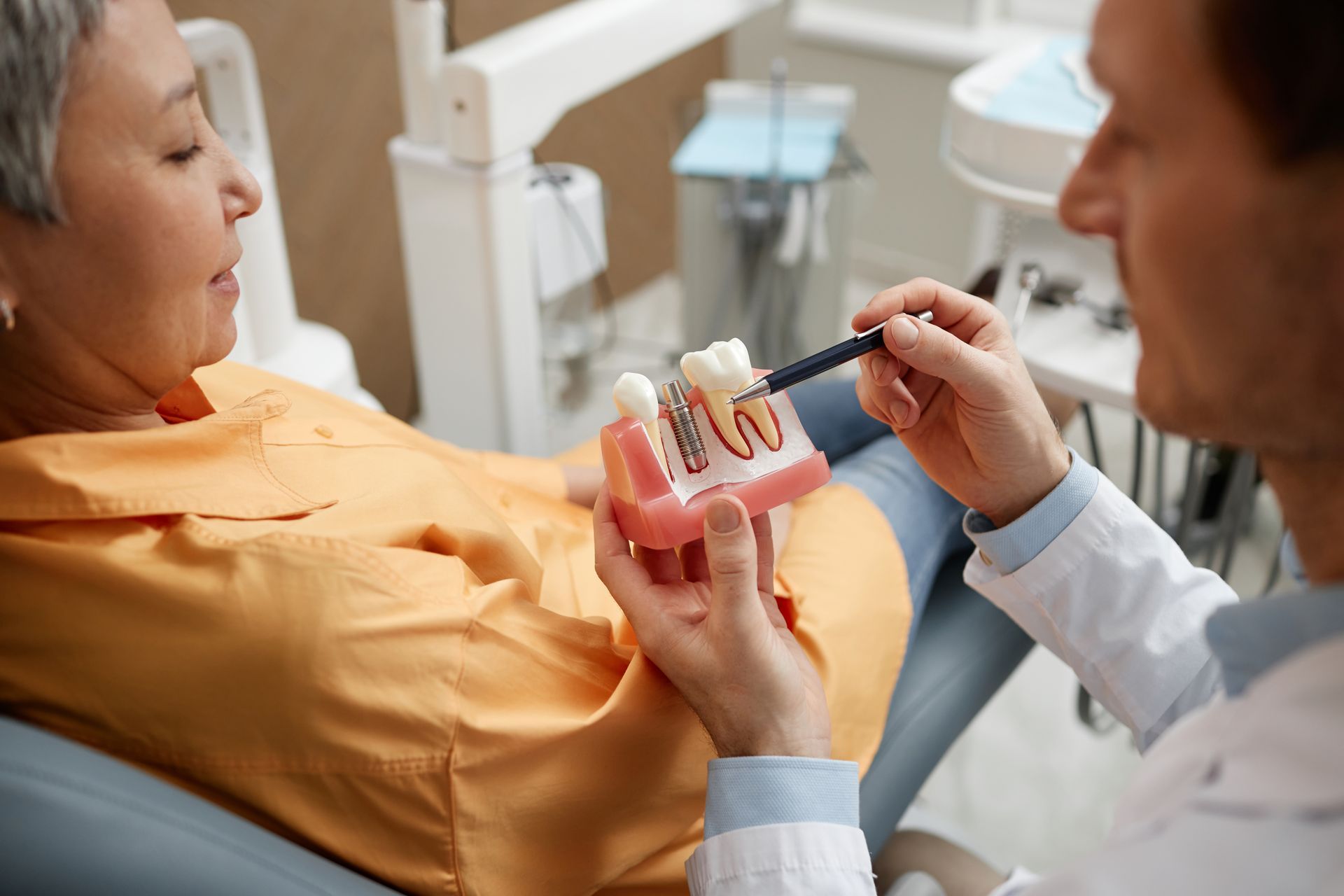 Dentist showing a dental model to a patient in a clinic, with instruments in hand