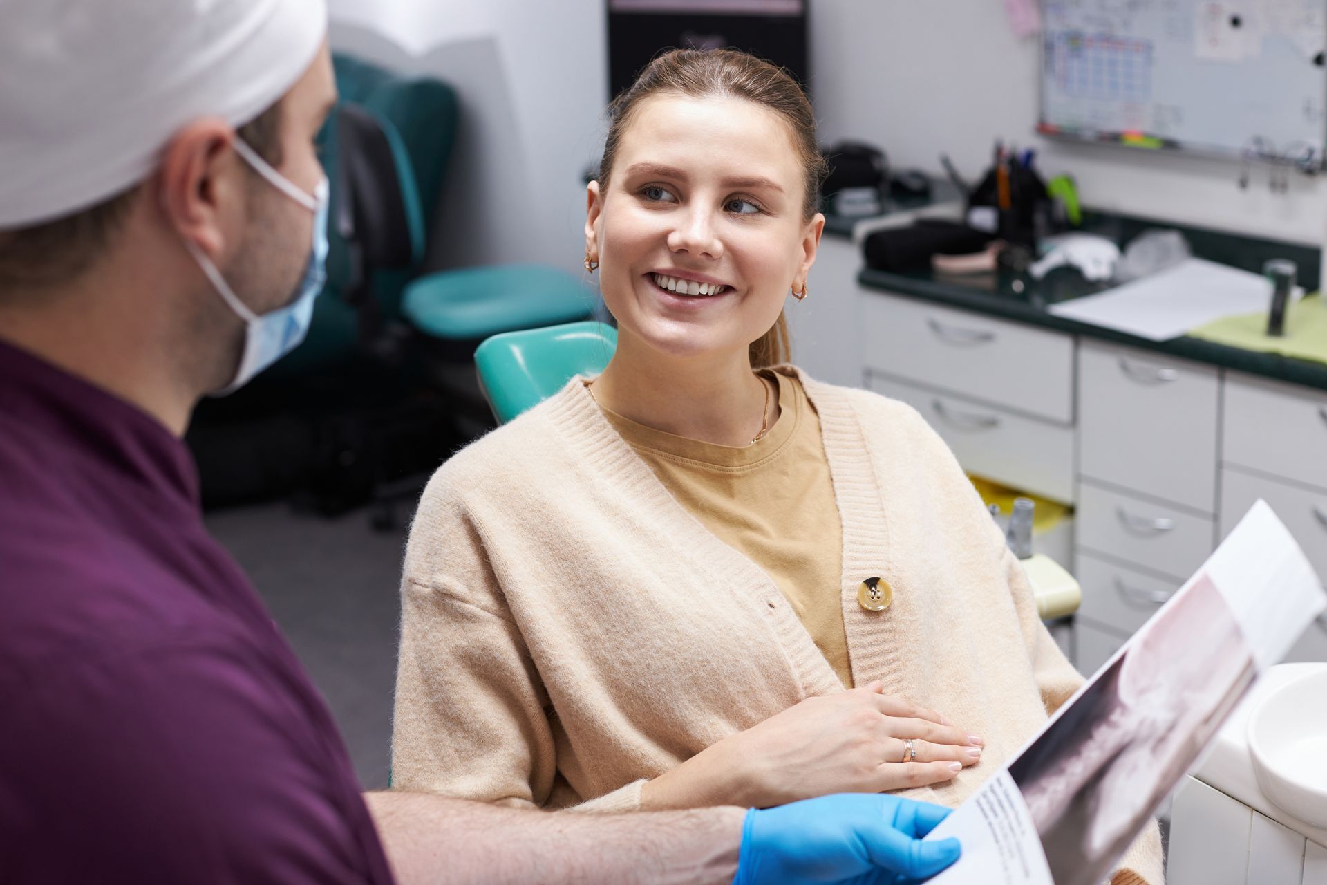 Dentist consulting a smiling patient in a clinic, with dental tools and paperwork on the desk.