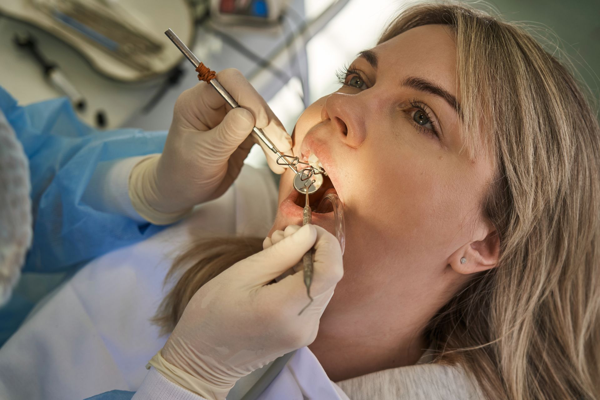 Dentist using a tool to examine a patient’s open mouth in a clinical setting