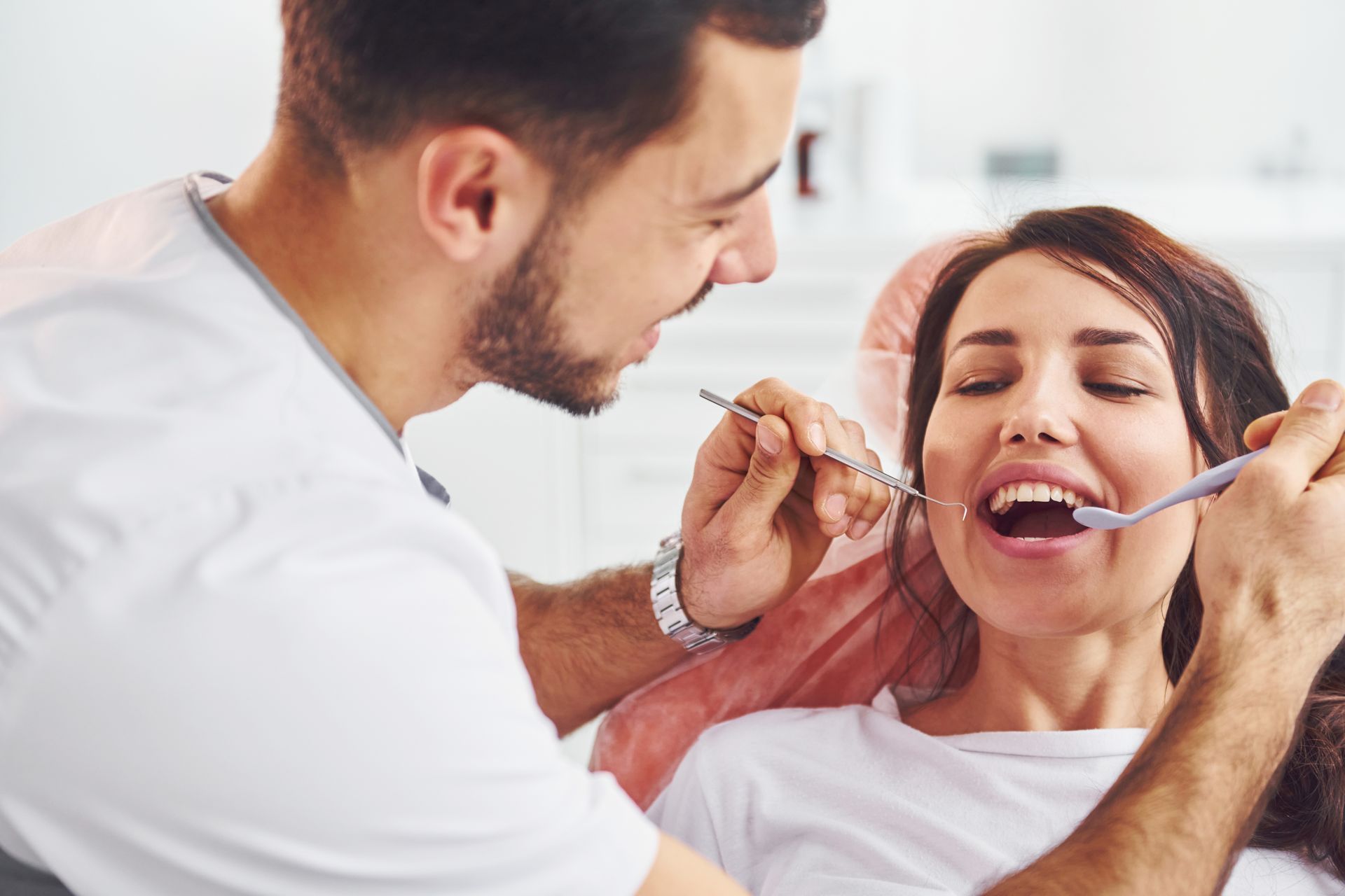 Dentist examining a smiling patient’s teeth with a mirror and probe in a clinic