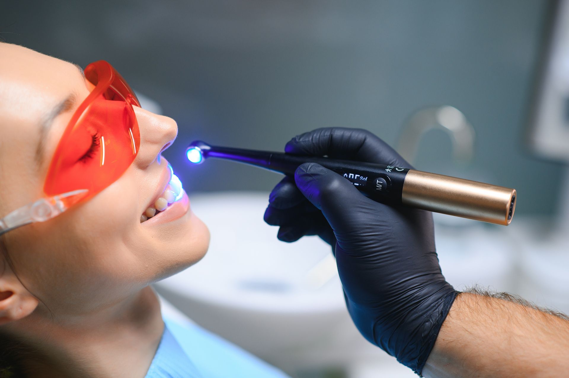 Dentist using a blue curing light on a patient wearing red protective glasses.