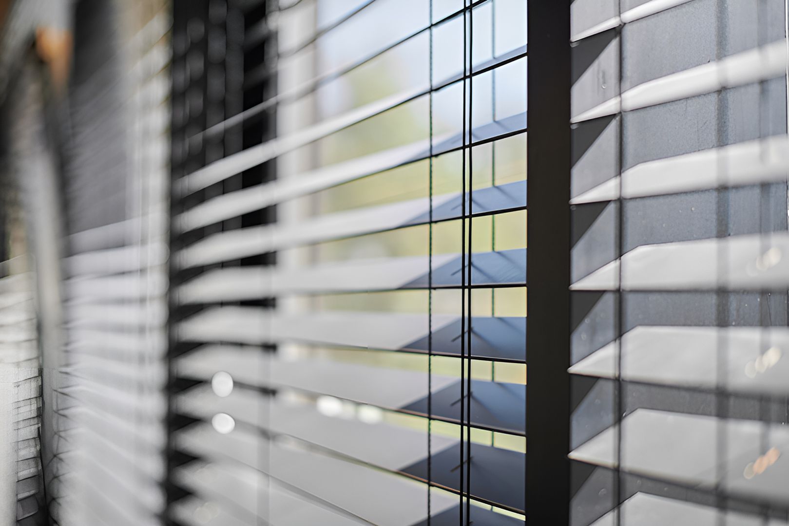 Close-up of grey horizontal window blinds with sunlight filtering through, creating shadows.