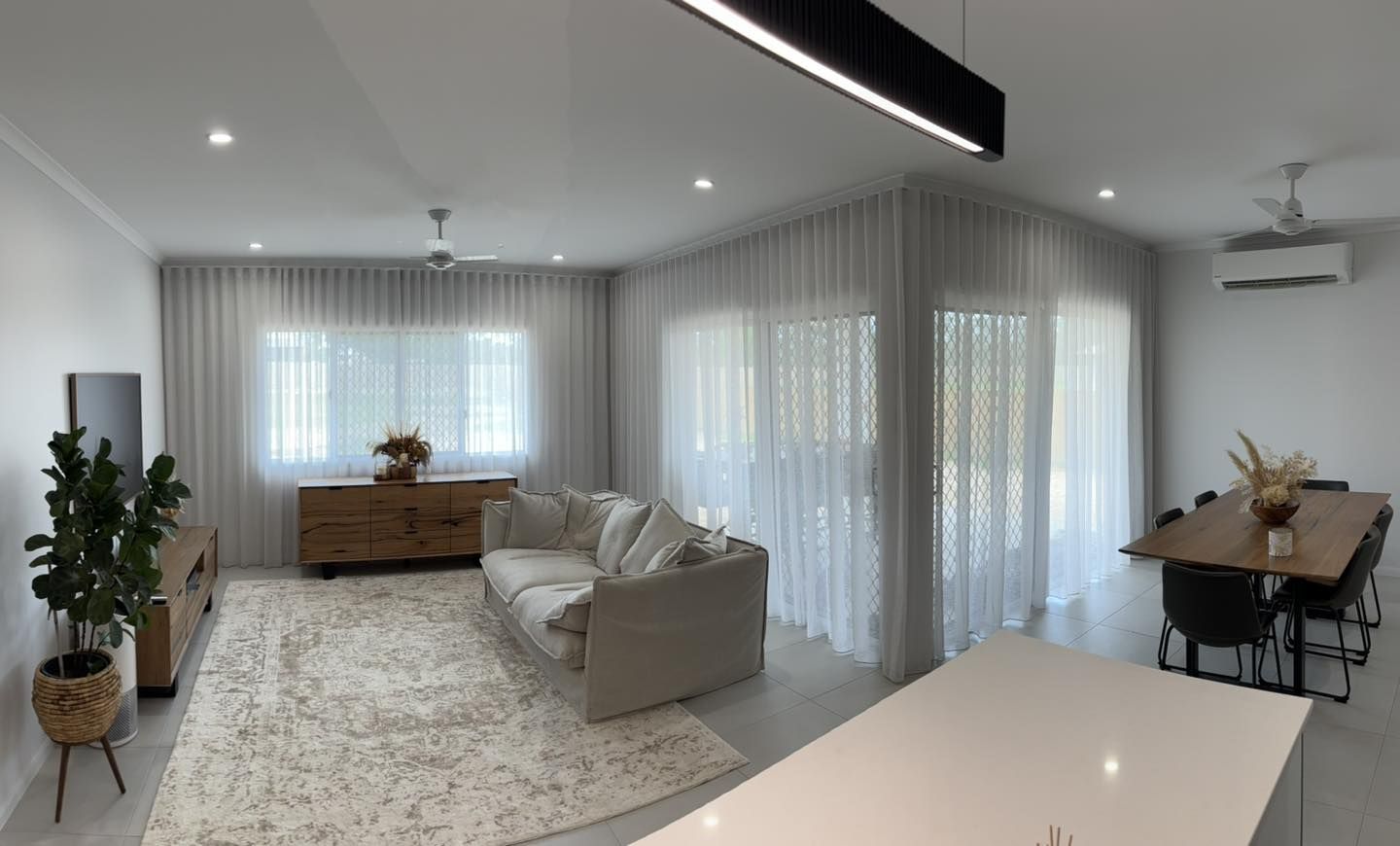 Modern living room with sheer white curtains, a neutral sofa, wooden furniture, and a dining area.