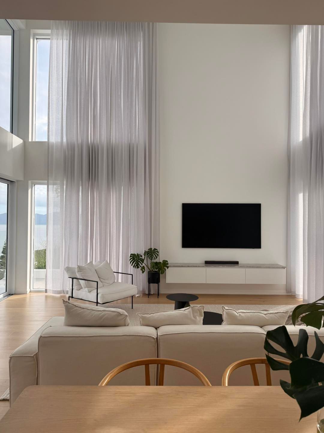 Sheer white curtains covering large windows and a dining area with shutters.
